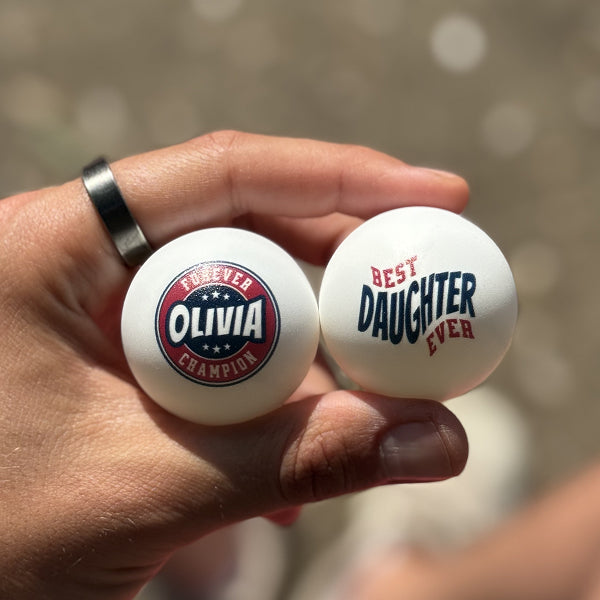 Fady holding two personalized ping pong balls with the name Olivia and 'Best Daughter Ever' design printed on them
