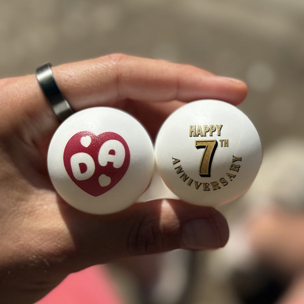 Fady holding two personalized ping pong balls with one showing a heart with 'DA' initials inside and the other 'Happy 7th Anniversary'
